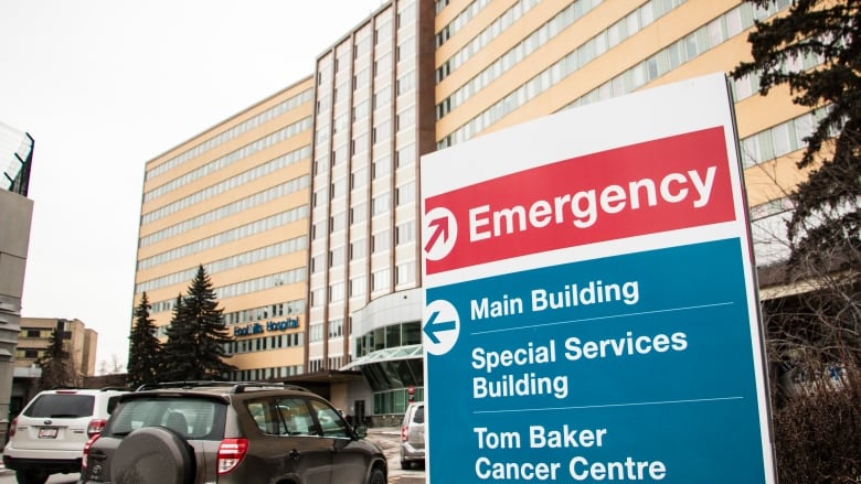 A sign with directions to the emergency department and main building is shown in front of a hospital.