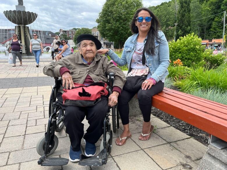 A woman sits on a bench alongside another woman in a wheelchair. 