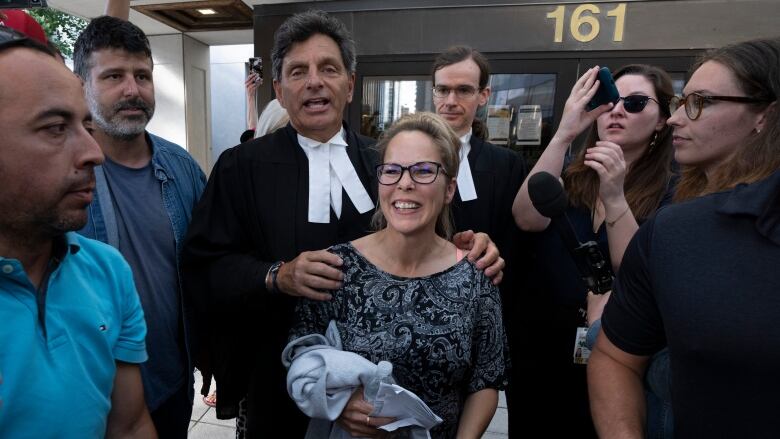 A woman smiles as her lawyer speaks behind her, surrounded by a few reporters and supporters.