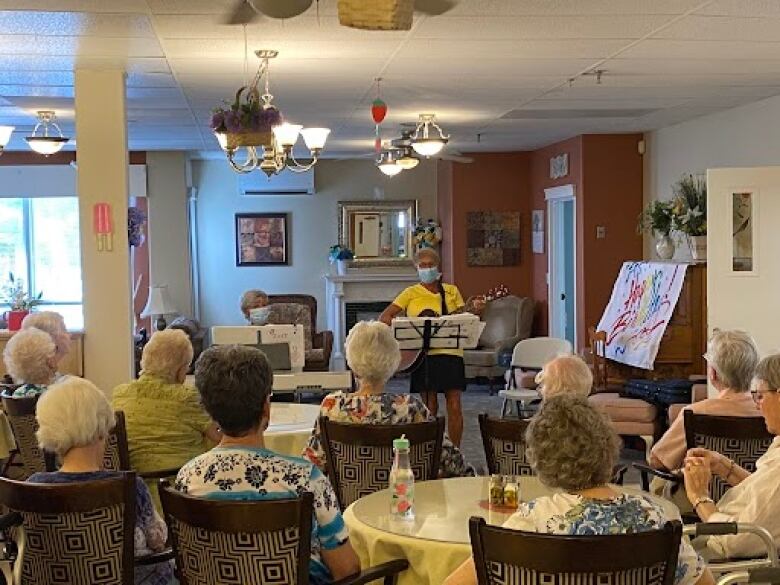 Two masked musicians perform for group of seniors at a seniors home.