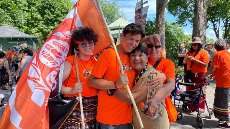 A group of people are hugging, smiling and carrying flags.