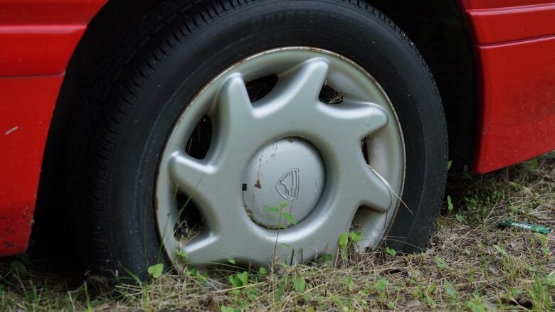 A close up picture shows a deflated dire on a red car, the wheel sunk into the ground.