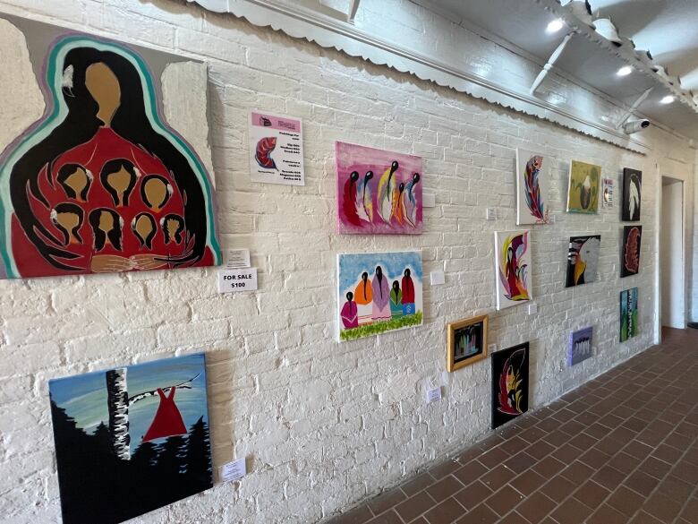 A collection of paintings hang on a white-brick wall.