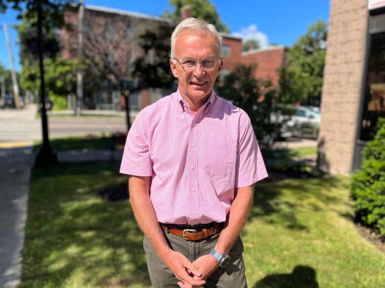 Sean Casey stands on Charlottetown street on a sunny summer day. He is wearing a short sleeved pink dress shirt. 