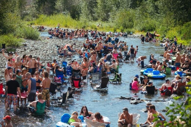 A number of people, many of them shirtless, gather along a riverbank.