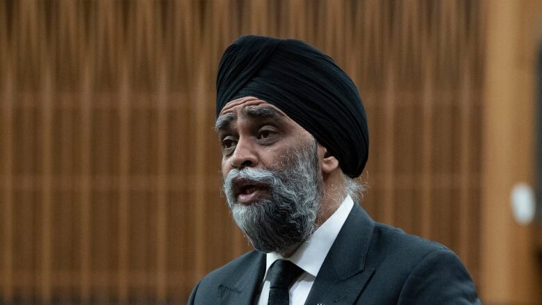 A man with a grey beard and black turban stands and speaks in the House of Commons.