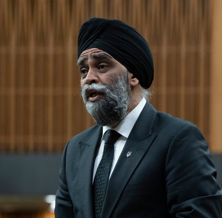 A man with a grey beard and black turban stands and speaks in the House of Commons.