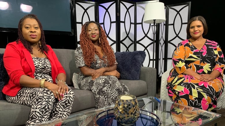 Three women sit on a TV set. 