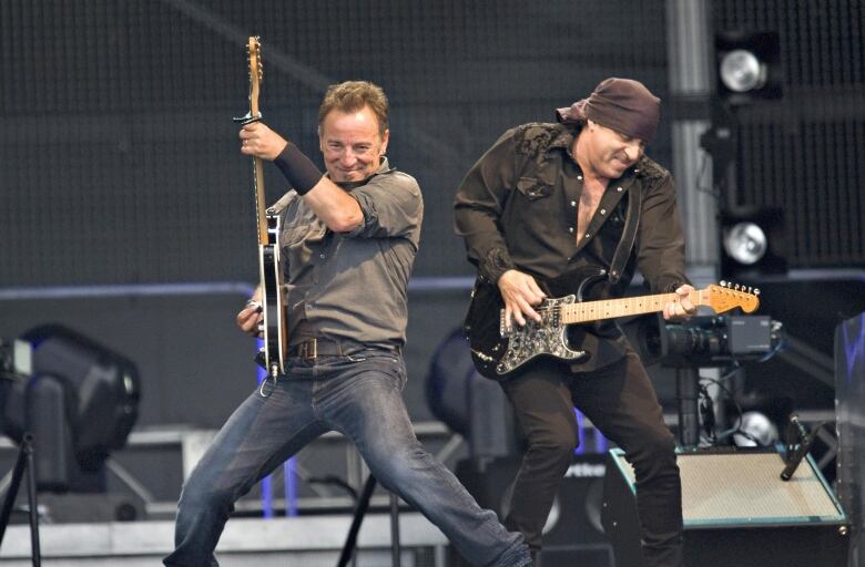 Two men with guitars perform energetically on a stage.