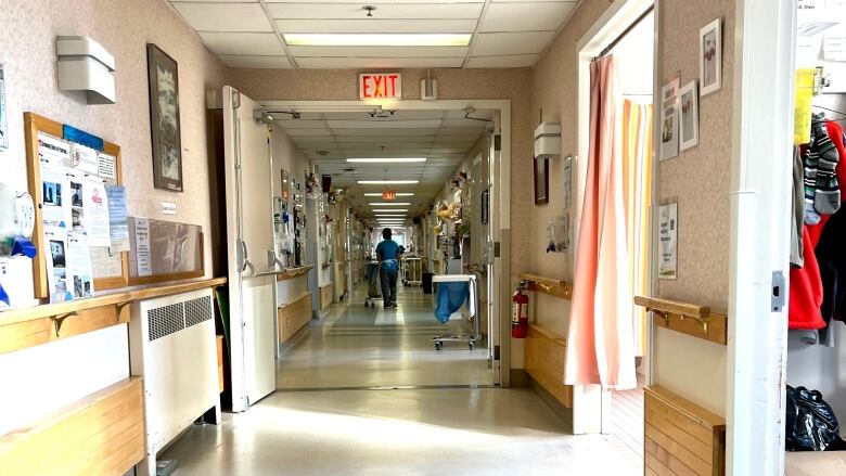 A long-term care worker is pictured at the end of a sunlit corridor. 