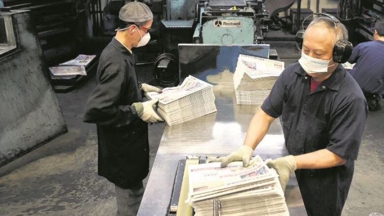 Two men arrange stacks of newspapers.