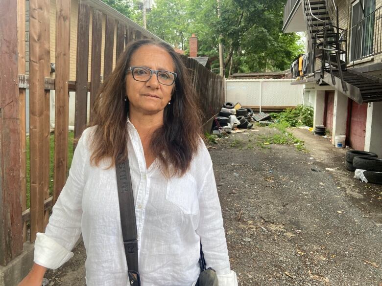 A woman stands behind an apartment building, where a pile of old tires can be spotted. 