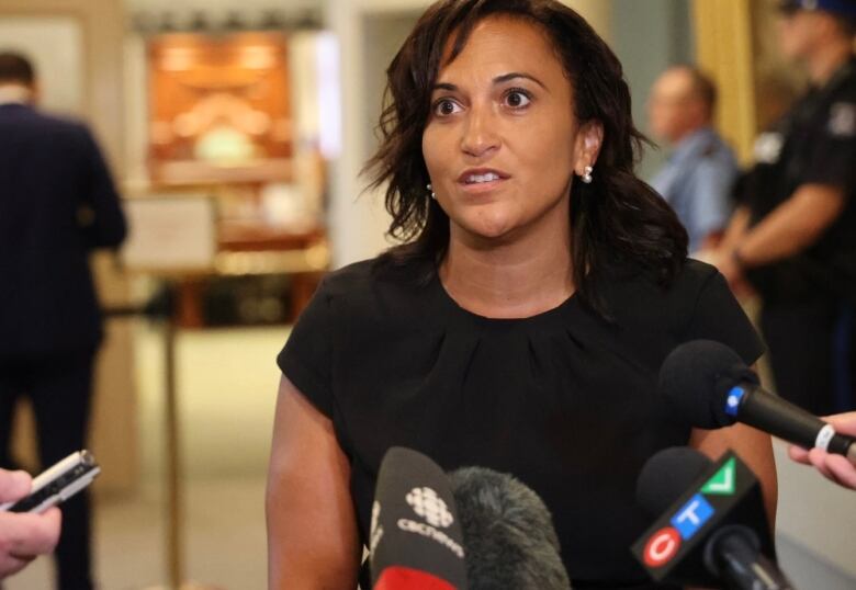 A Black woman wearing a black top is while speaking into reporter's mics