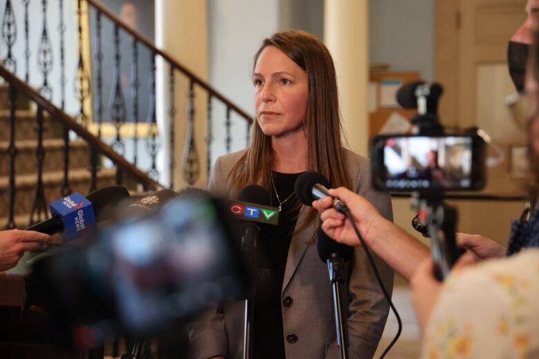 A woman stands in front of a media scrum.