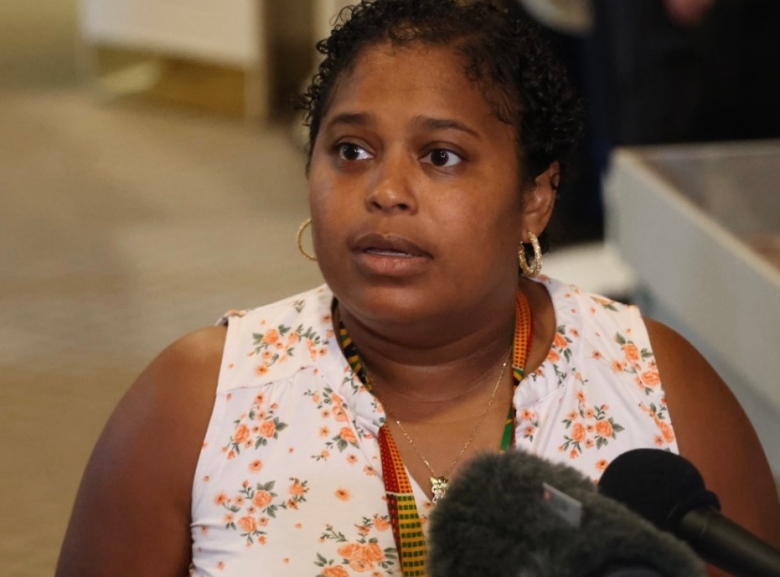 A Black woman with short curly hair wearing a white top