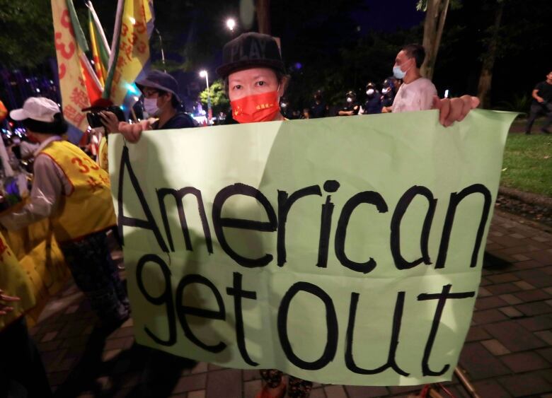 A protester holds a banner that reads, 'American Get Out.'