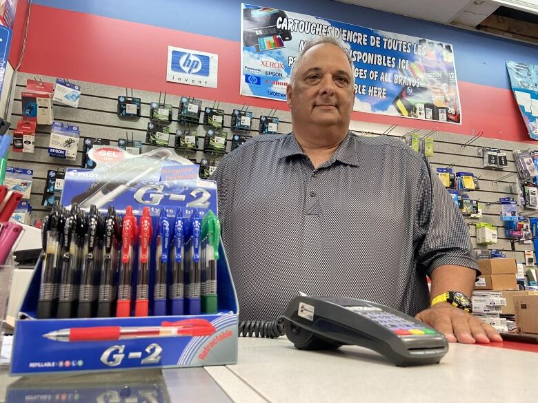 A man stands behind a counter that has school supplies.