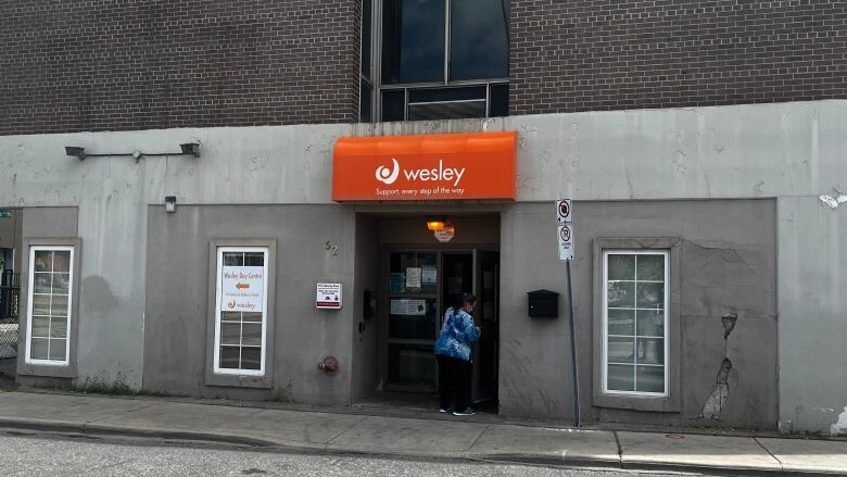 A beige building with a woman in blue scrubs entering. Above, an orange sign that says 'Wesley: Support every step of the way'.