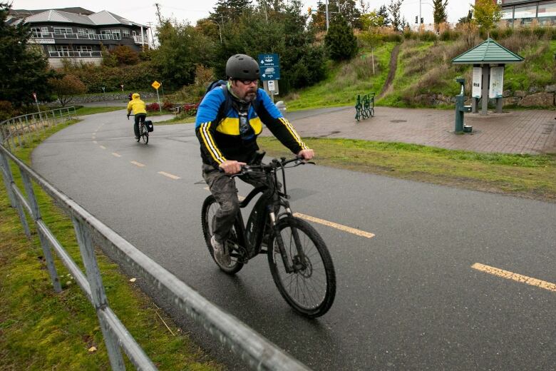 A male cyclist rides an e-bike on a paved trail.