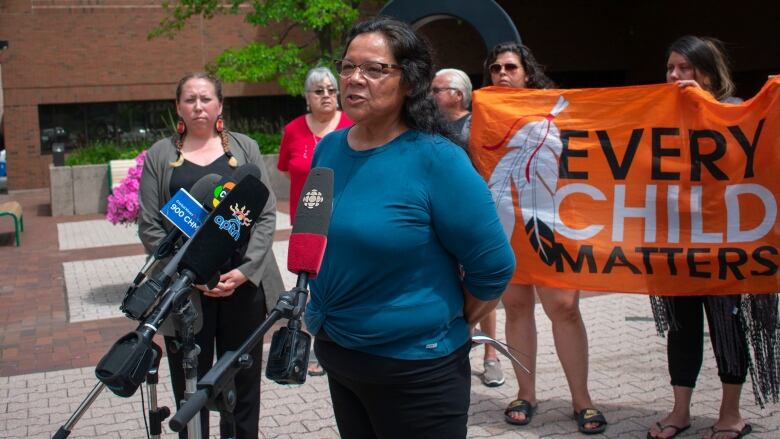 A woman stands and speaks into microphones