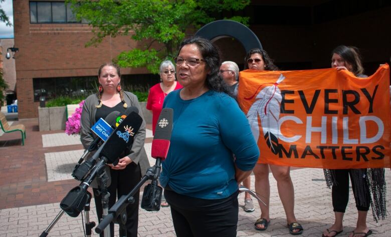 A woman stands and speaks into microphones