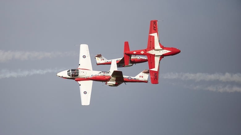 Two planes with red-coloured wings pass each other in the sky.