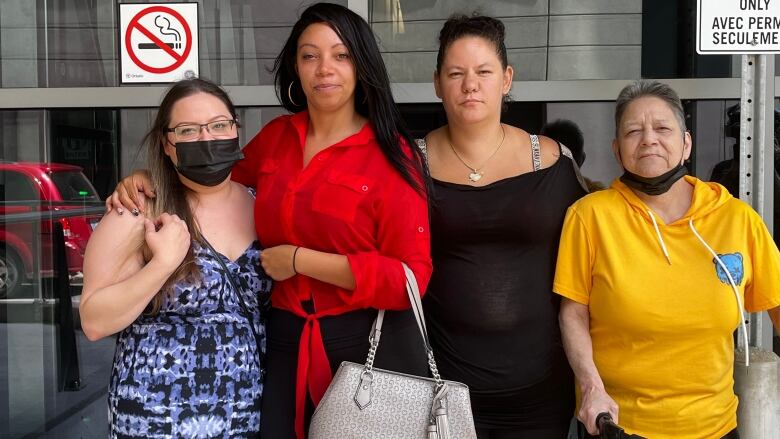 Four Indigenous women stand in front of a courthouse window. 