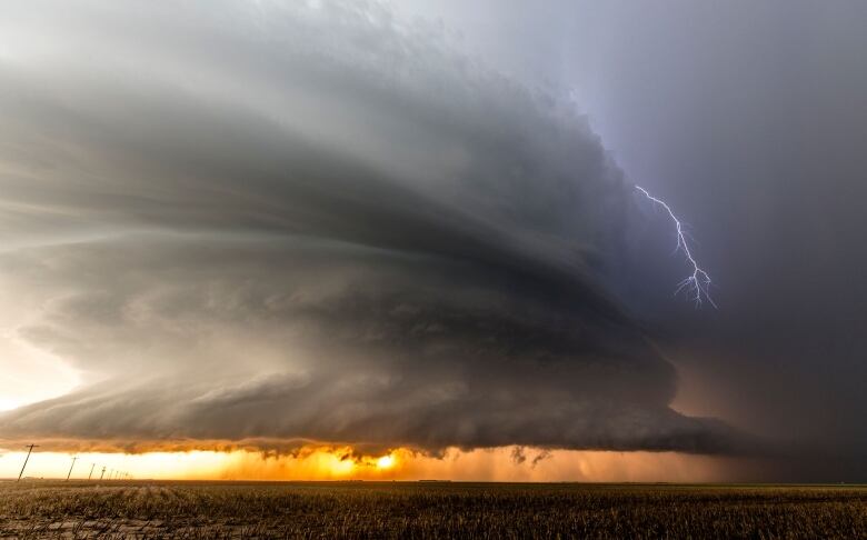 a large cloud and a lightning strike over a field