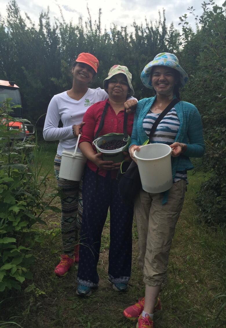 Three women hold buckets filled with Saskatoon berries.