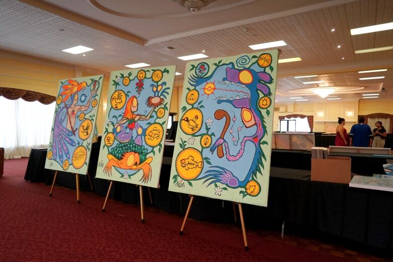 Several canvases of Indigenous art stand on display in a room.