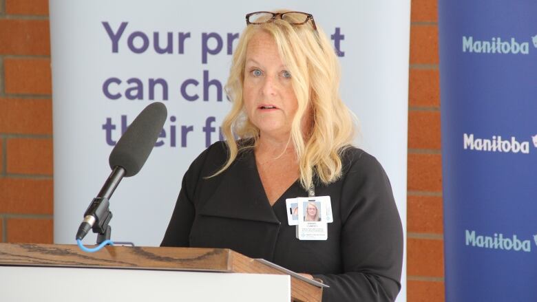 A woman wearing ID tags on her shirt and glasses on her head speaks at a podium.