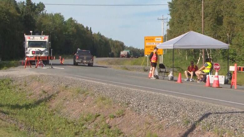 A checkpoint on the highway keeping the road closed to traffic, with people in safety vests sitting by the side of the road.