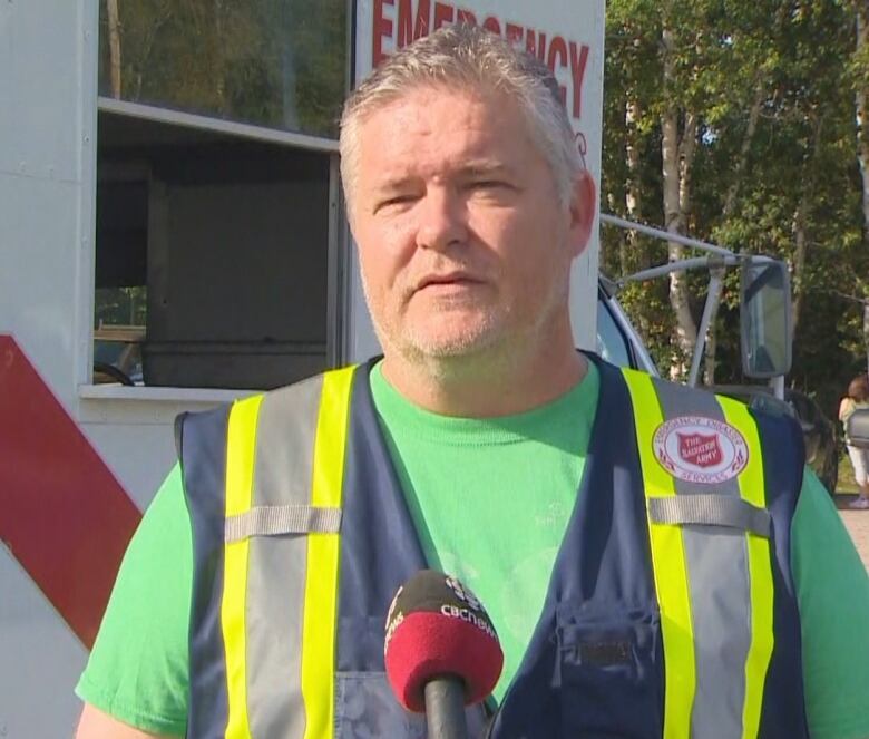 A middle-aged man looks into the camera. He's wearing a safety vest and stands next to a vehicle that has 