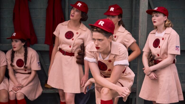 A screengrab showing actors in the 'A League of their Own', who are all women in a baseball dugout wearing salmon-coloured uniforms.