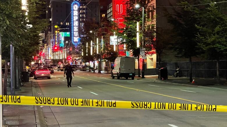 A police officer walks on a closed-off street with hoardings and neon signs visible behind them.