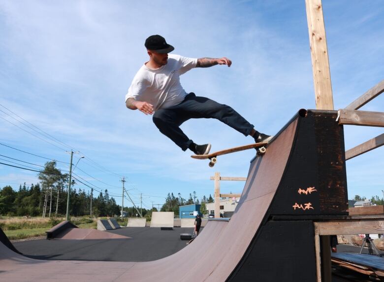 A young man balances himself on a skateboard as it crests near the top of a ramp. 