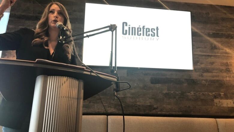 Tammy Frick, the executive director of Cinefest and Cultural Industries Ontario North, stands at a podium in front of a Cinefest logo. 