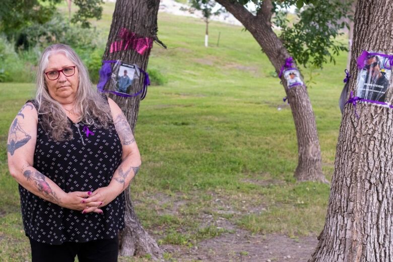 A woman stands by trees with purple ribbons representing overdose deaths.