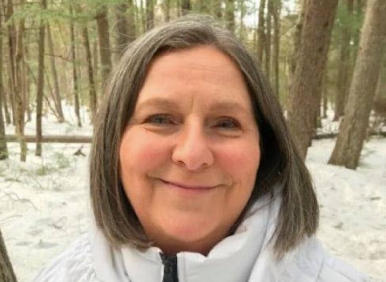 Smiling woman in parka in woods.