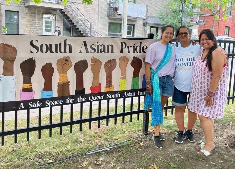 Three people smile beside a banner that reads South Asian Pride.