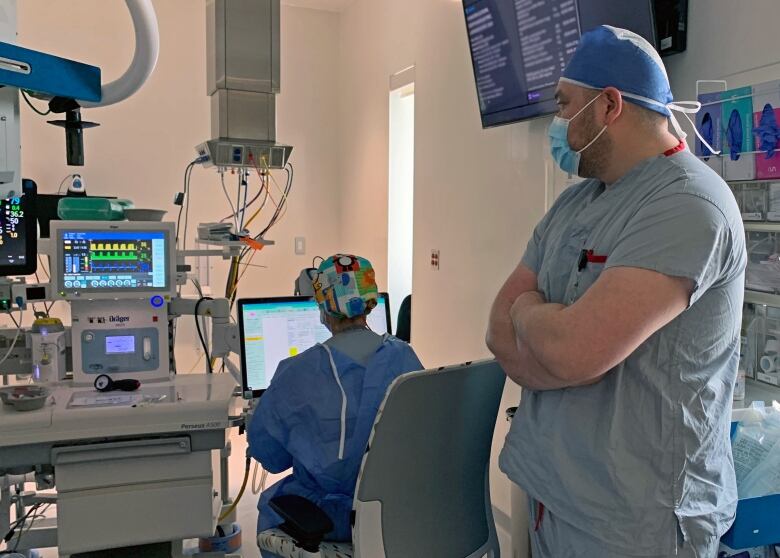 Two doctors in hospital gowns and masks look over medical monitors.