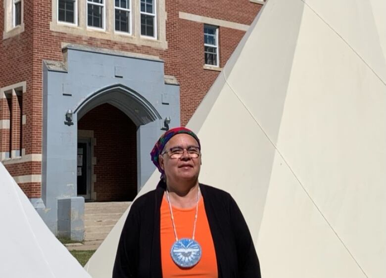 The university president, wearing an orange shirt, stands in front of the school.