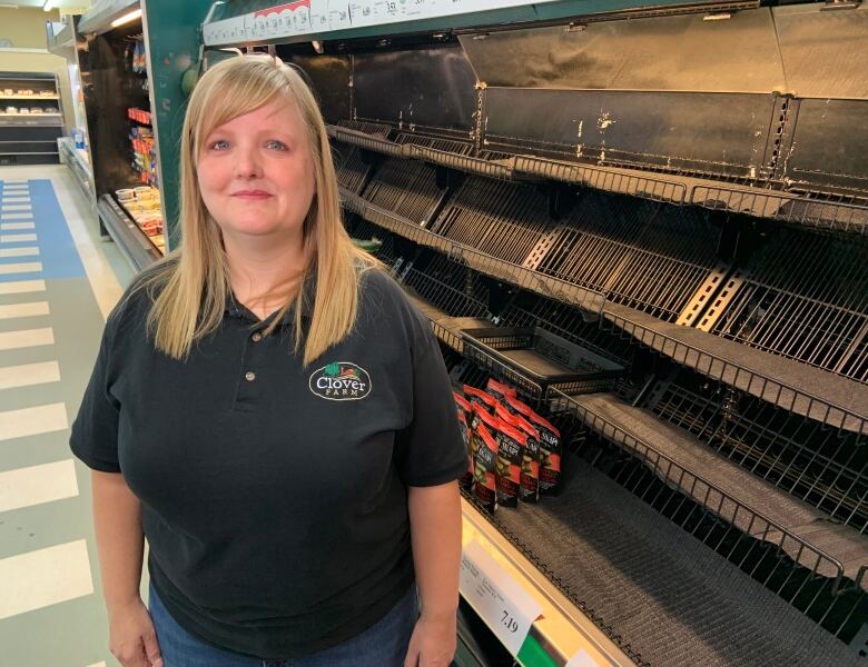 A person stands in front of an empty grocery store shelf.