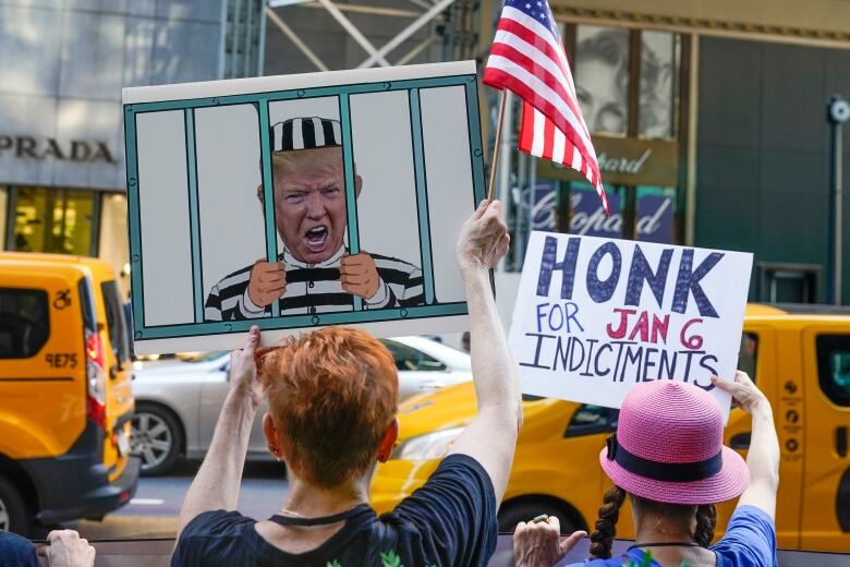 Two people hold up protest signs on a city sidewalk.