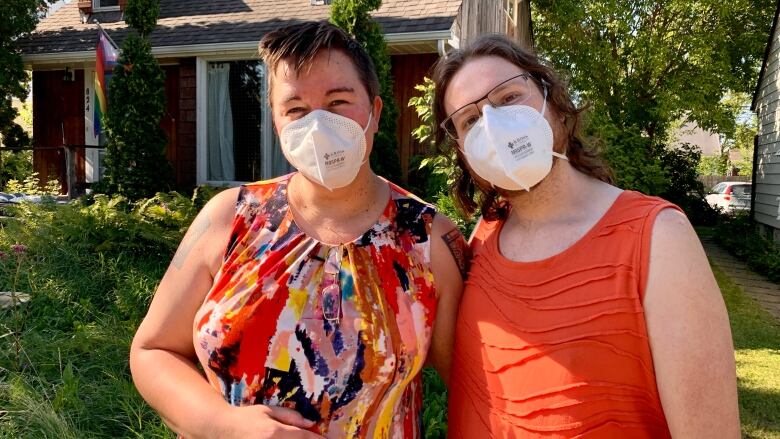 Two people wearing face masks stand in front of a house.