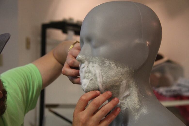 A makeup artist applies liquid latex to a prosthetic head 