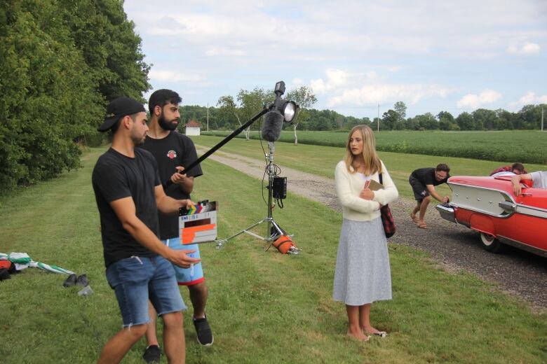 An actress stands under a boom mic as two crew members get ready to shoot a scene