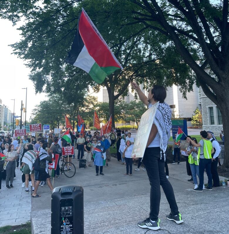 A man waves a Palestinian flag in front of a crowd of people.