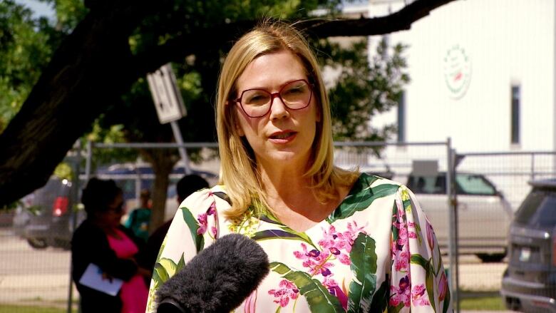 A woman in a floral shirt speaks into a microphone.