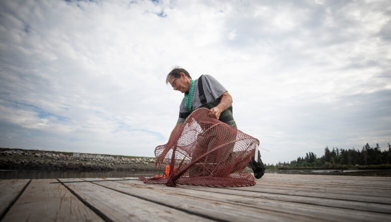 A man holds a netted trap while crouching on a dock.